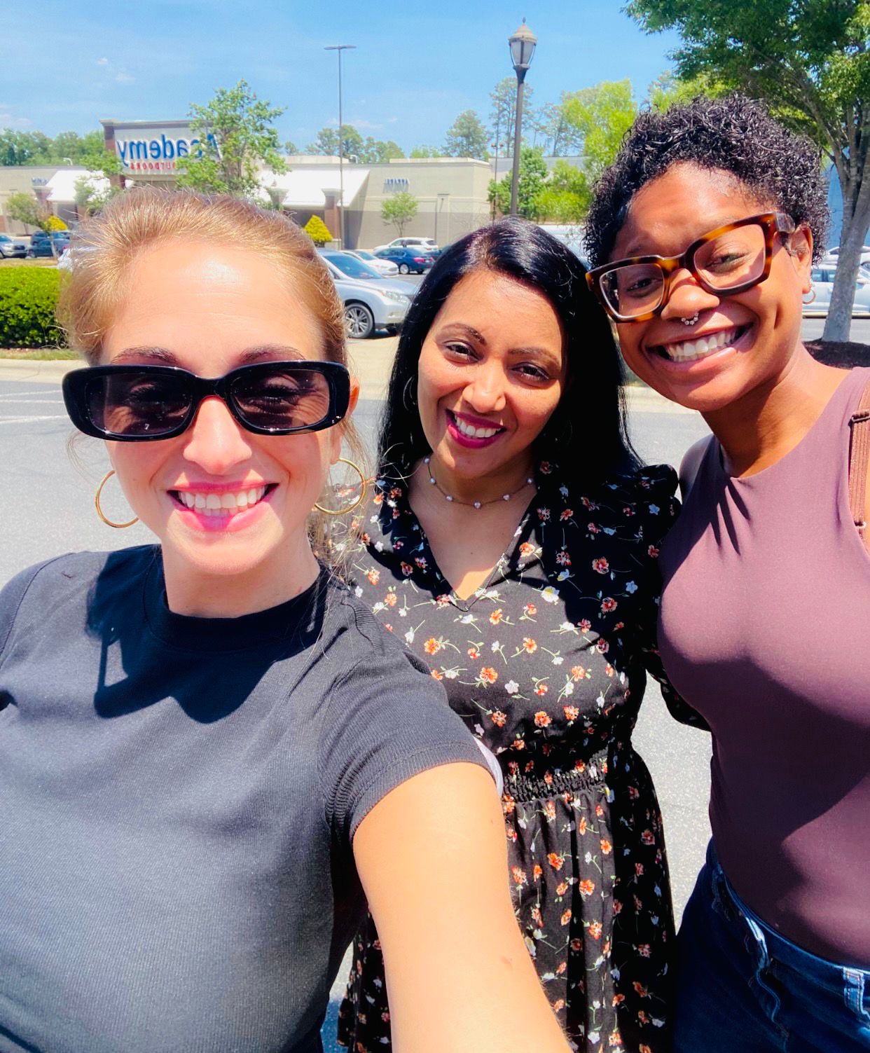 Three women smiling together outdoors beside a building
